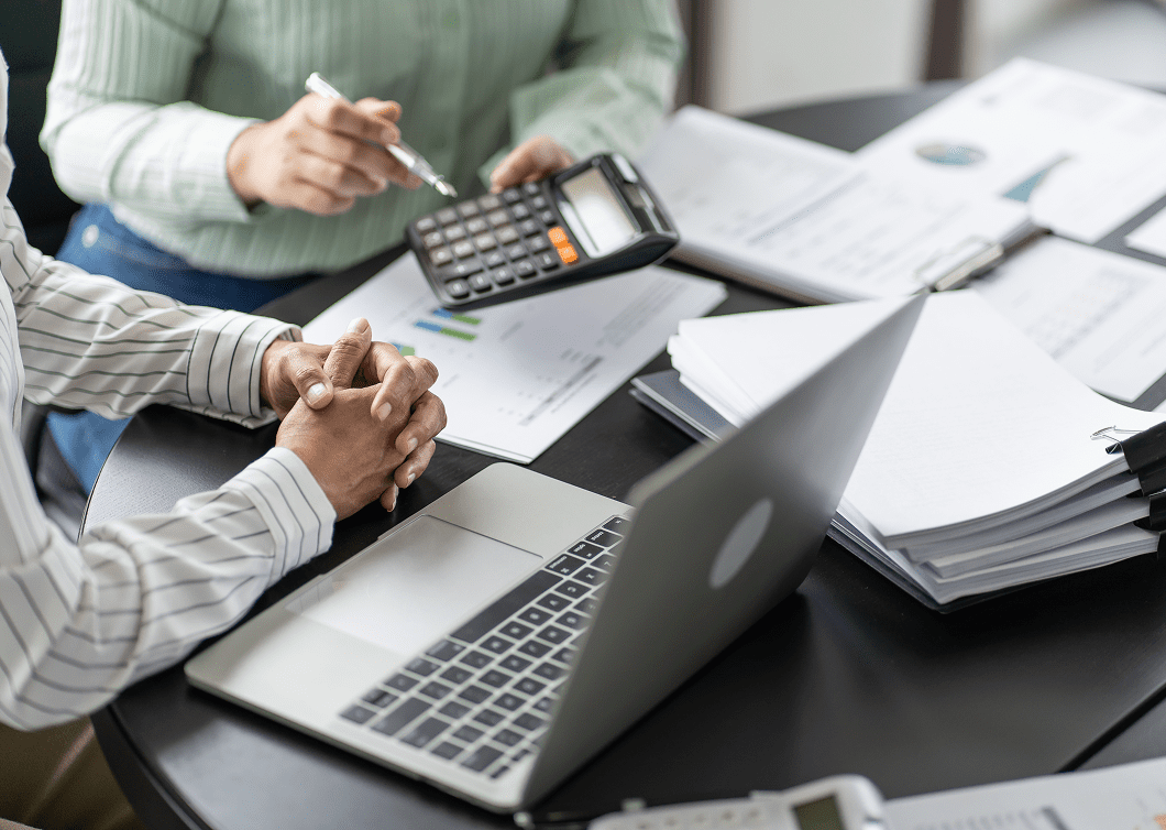 Two people working on finances with calculator, laptop, and documents.