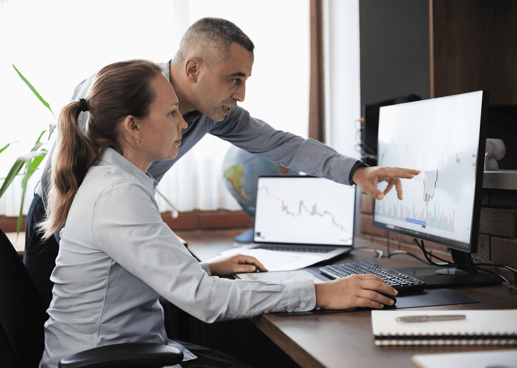 Two professionals analyze data on computer screens in an office.